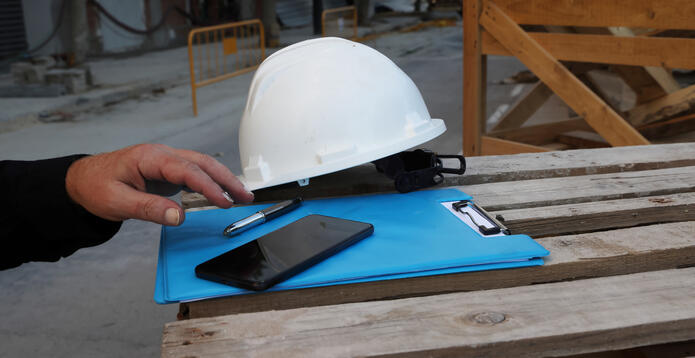 Safety hard hat, clipboard, pen and smartphone at a construction site