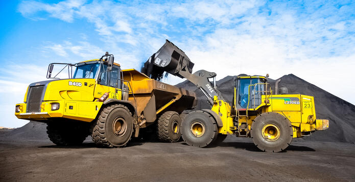 Yellow dump truck being loaded by a large excavator at a quarry site