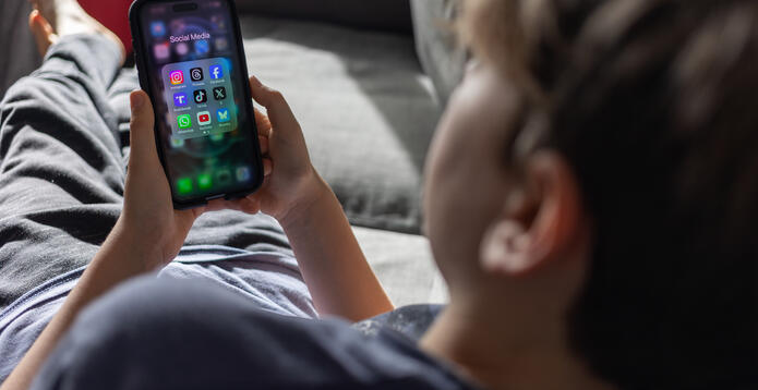 A child lying down on a sofa plays with a smartphone