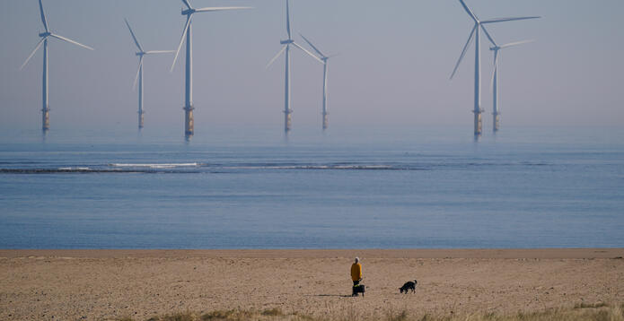 A woman walks her dog on the beach in front of the EDF energy offshore wind farm at South Gare near Redcar on March 20, 2025 in Redcar, United Kingdom.