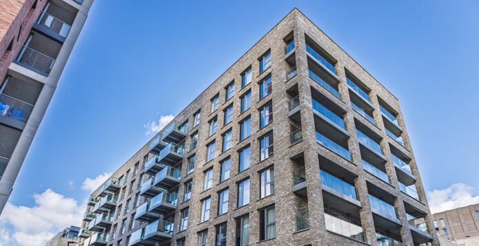 Modern brick apartment building with glass balconies under a blue sky