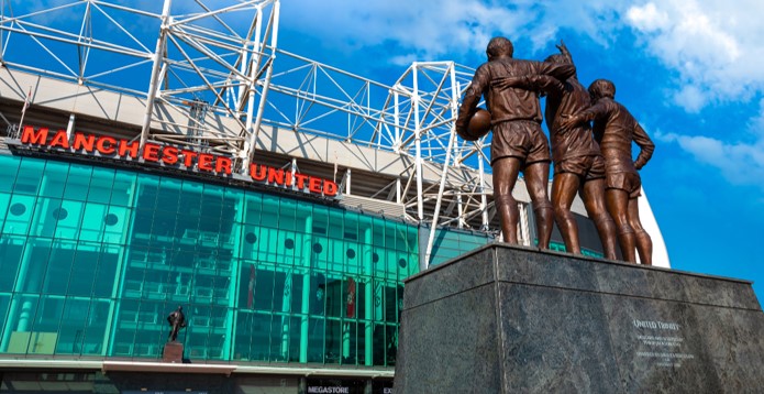 United Trinity bronze statue outside MUFC Old Trafford stadium against blue sky