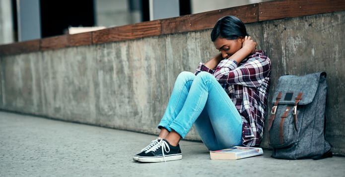 Young female student sitting on the floor feeling depressed outside on campus