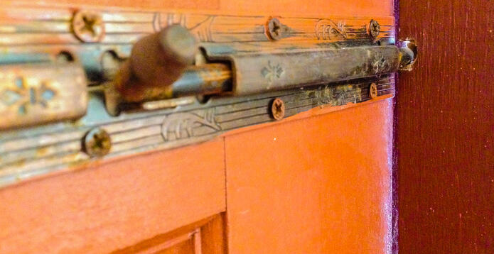Closeup a brass latch on a wooden door to slide to the drilled hole to lock interside the house. Photo: iStock
