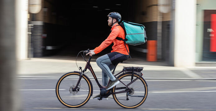 Cyclist delivering food with backpack riding through city street