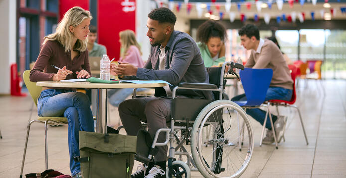 Two College Or University Students With One In Wheelchair Working Together In Study Area