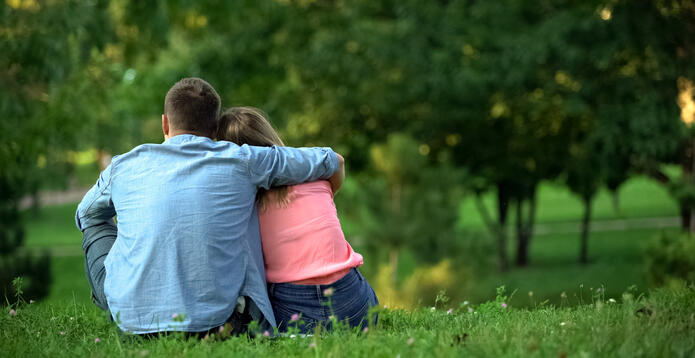 Loving male and female hugging sitting on grass in park