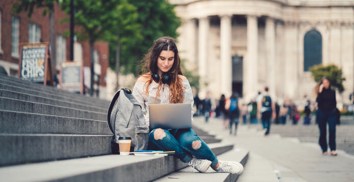 Student with laptop on steps with blurred background