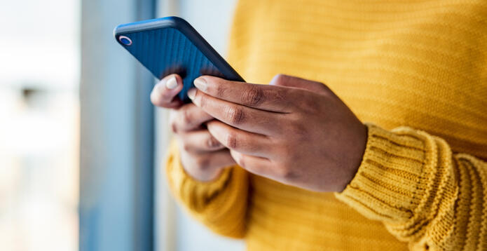 The hands of an adult wearing a yellow sweatshirt holding a smartphone