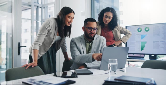 A group of colleagues brainstorming in an office. There is a screen displaying some charts in the background.