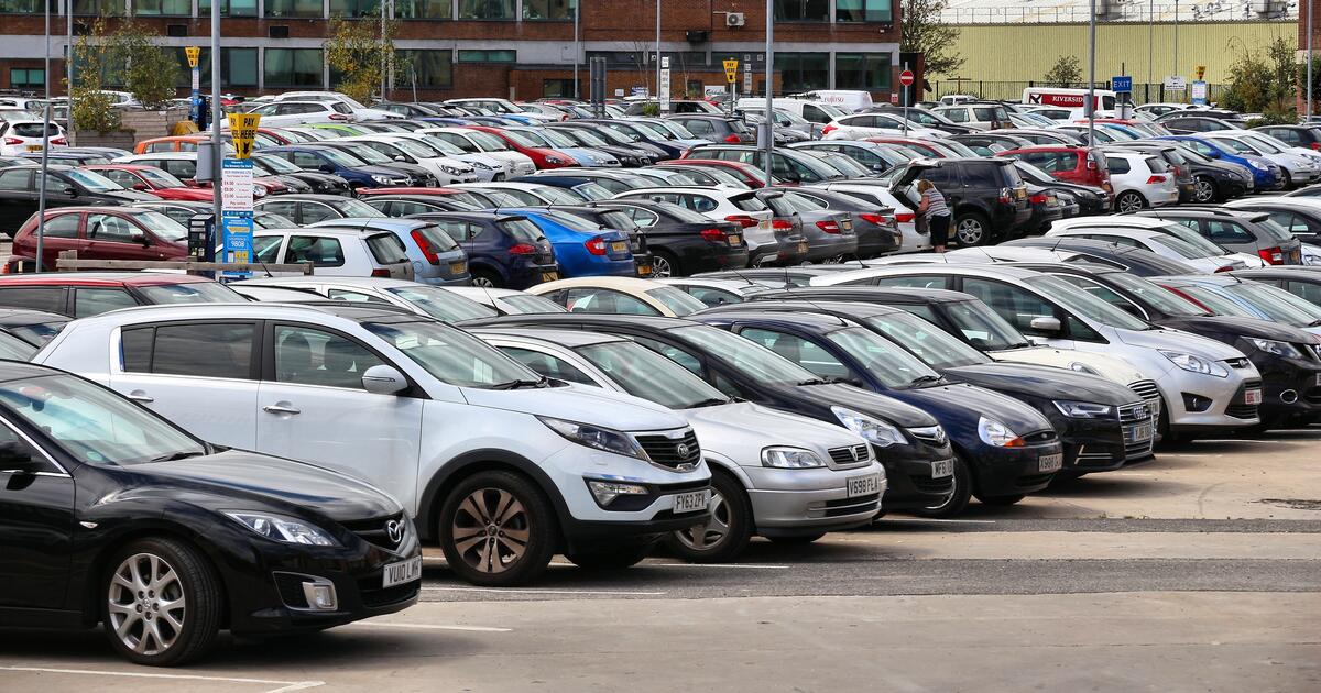 Large outdoor car park filled with rows of parked vehicles near commercial buildings