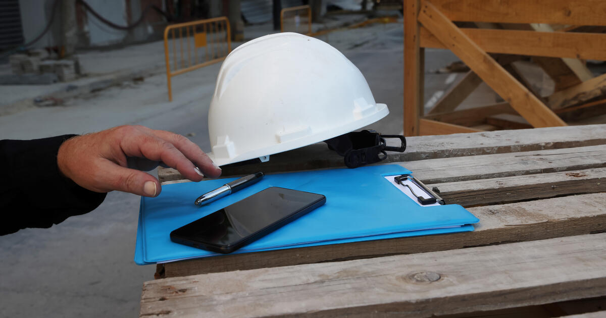 Safety hard hat, clipboard, pen and smartphone at a construction site