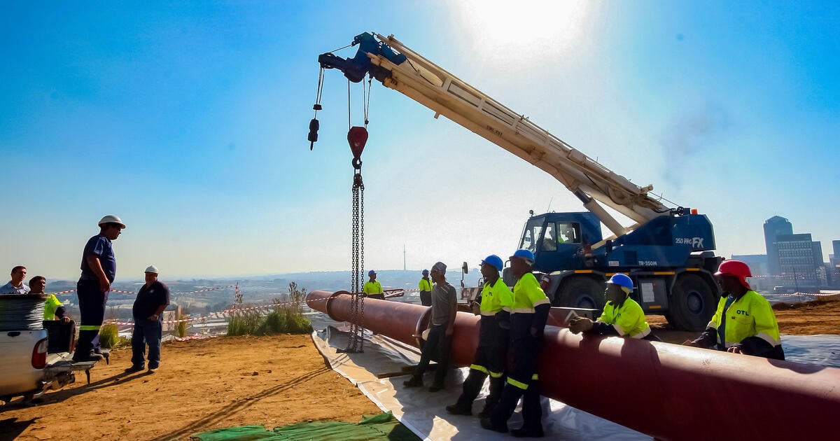 Construction workers helping Heavy duty construction crane lifting steel pipe on a building site