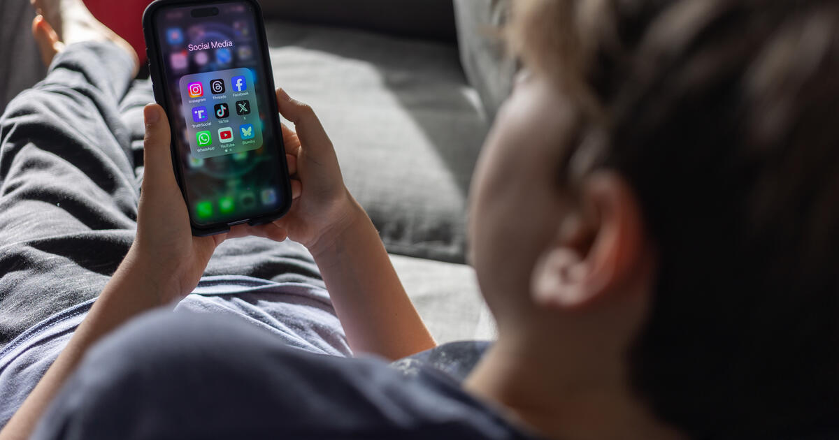 A child lying on a sofa plays with a smartphone