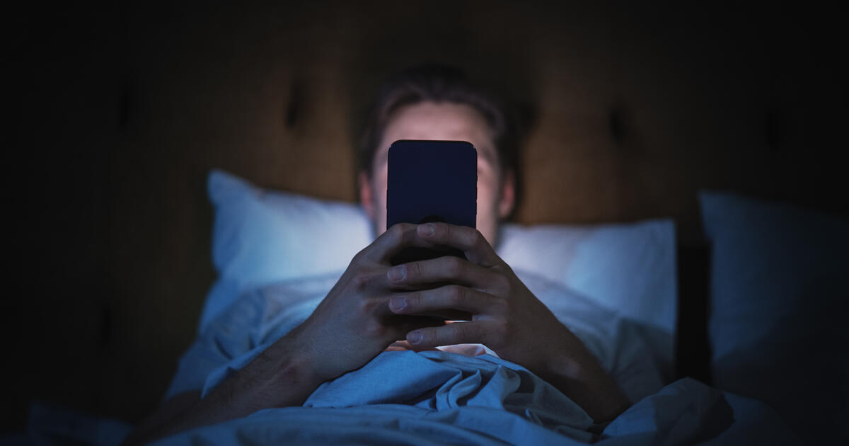 Man scrolling on phone in bed at night