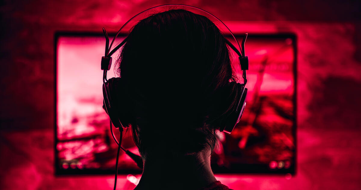 Red illuminated gamer wearing headset face screen