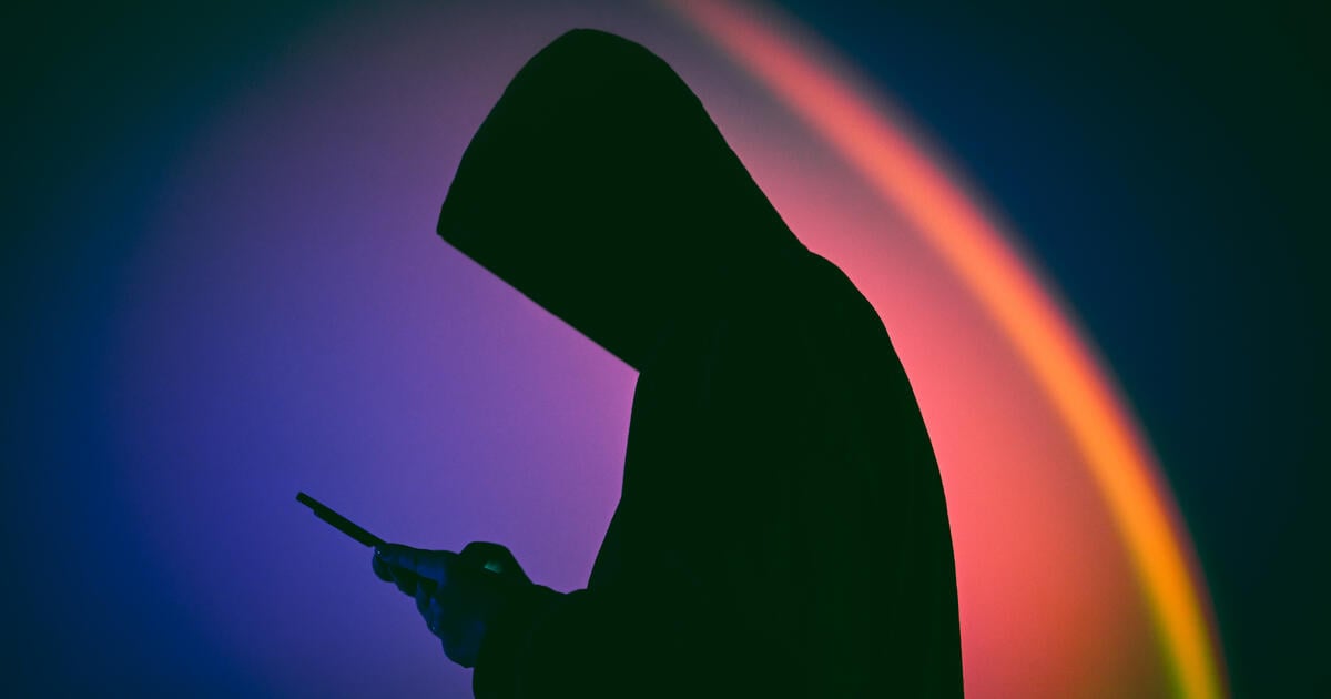 Silhoutted hooded hacker on mobile device