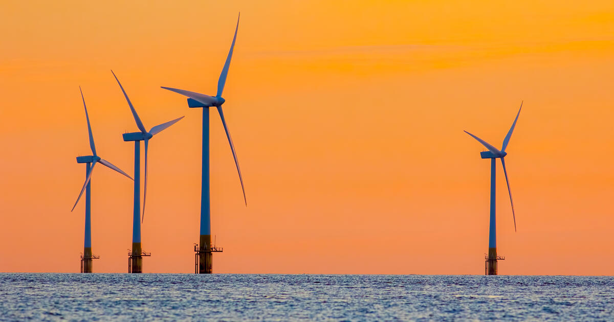Offshore wind turbines at sea silhouetted against an orange sky