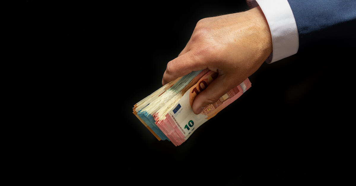 Hand holding a bundle of euro banknotes against a black background