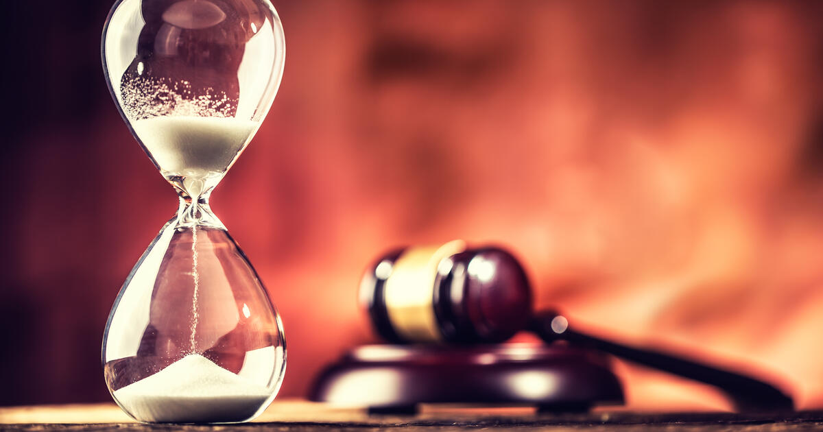 Modern hourglass in running time and justice hammer on wooden table.