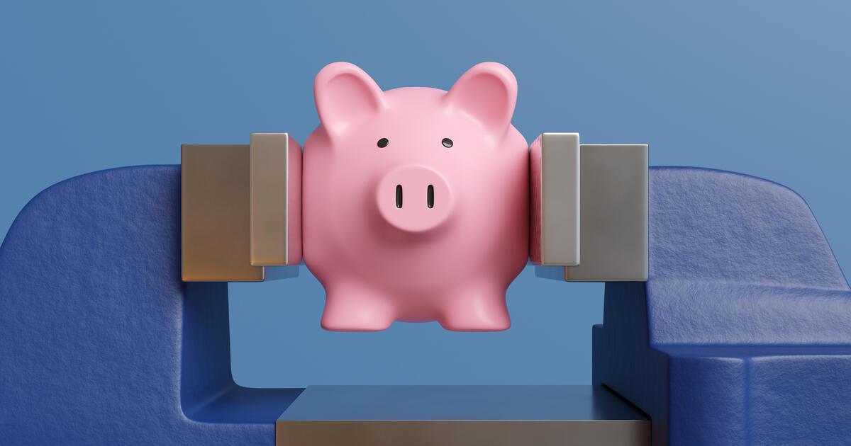 Pink piggy bank being pressed and crushed by a blue vice