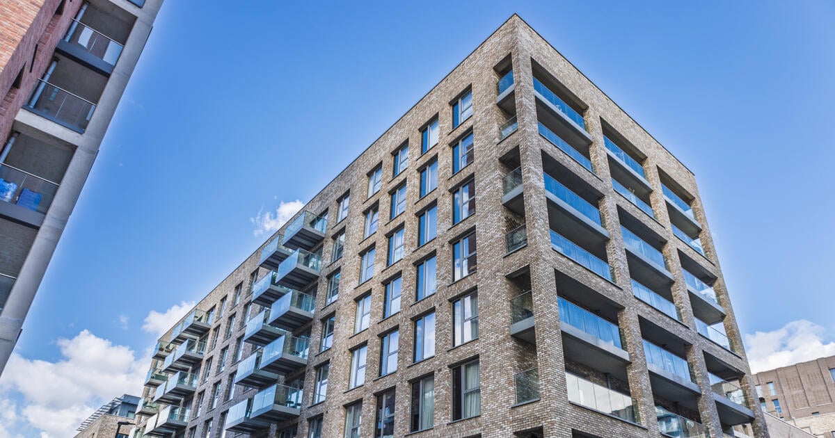 Modern brick apartment building with glass balconies under a blue sky