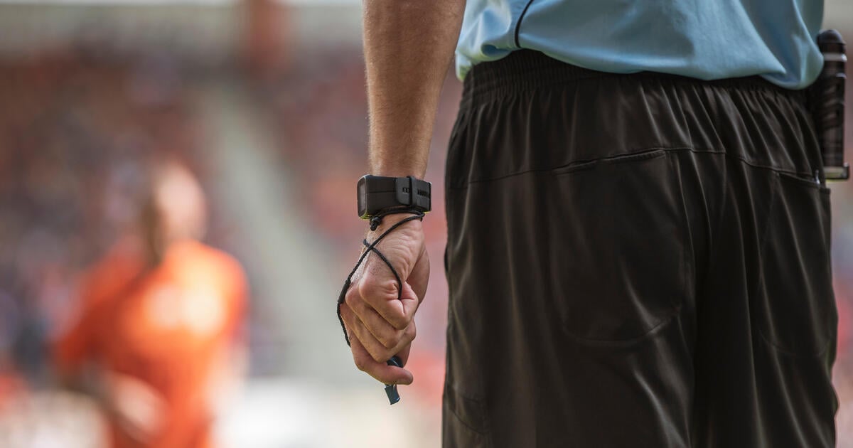 Hand of soccer referee with wristwatch and whistle.