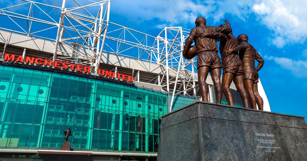 United Trinity bronze statue outside MUFC Old Trafford stadium against blue sky