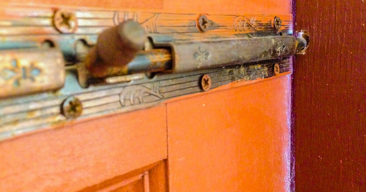 Closeup a brass latch on a wooden door to slide to the drilled hole to lock interside the house. Photo: iStock
