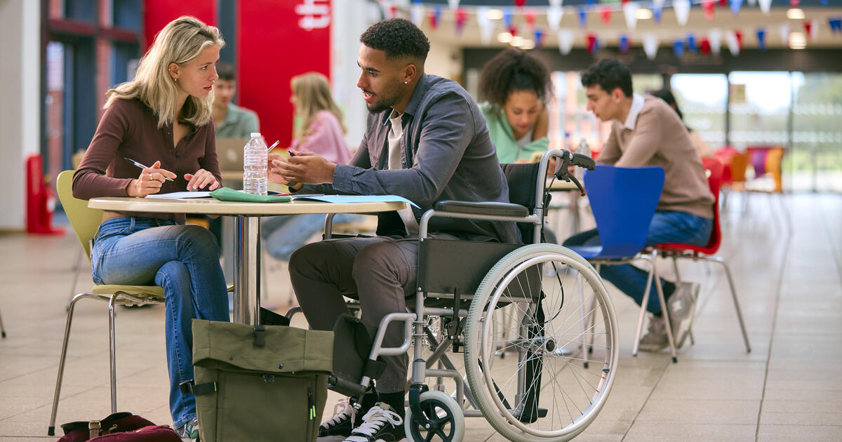 Two College Or University Students With One In Wheelchair Working Together In Study Area