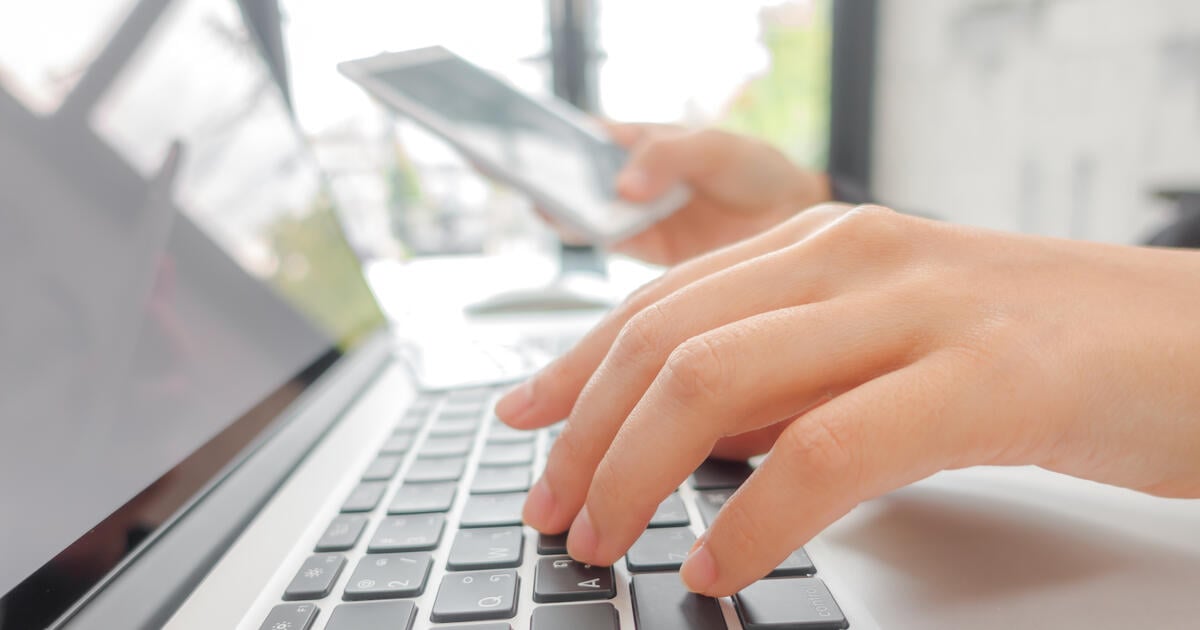 Closeup of business woman hand typing on laptop keyboard with mobile phone