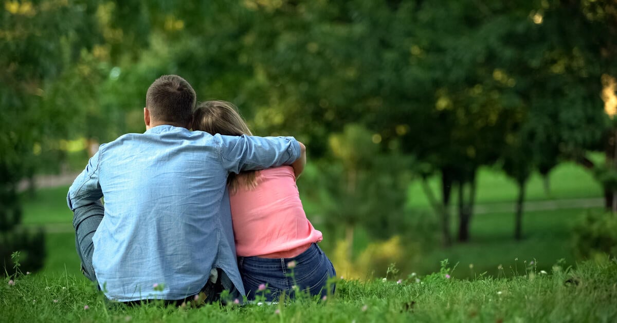 Loving male and female hugging sitting on grass in park 