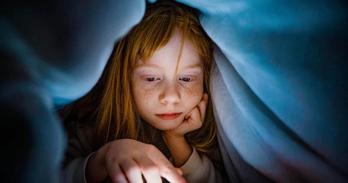 Red haired girl using phone under bed covers_Digital - SEOSocialEditorial image (1)