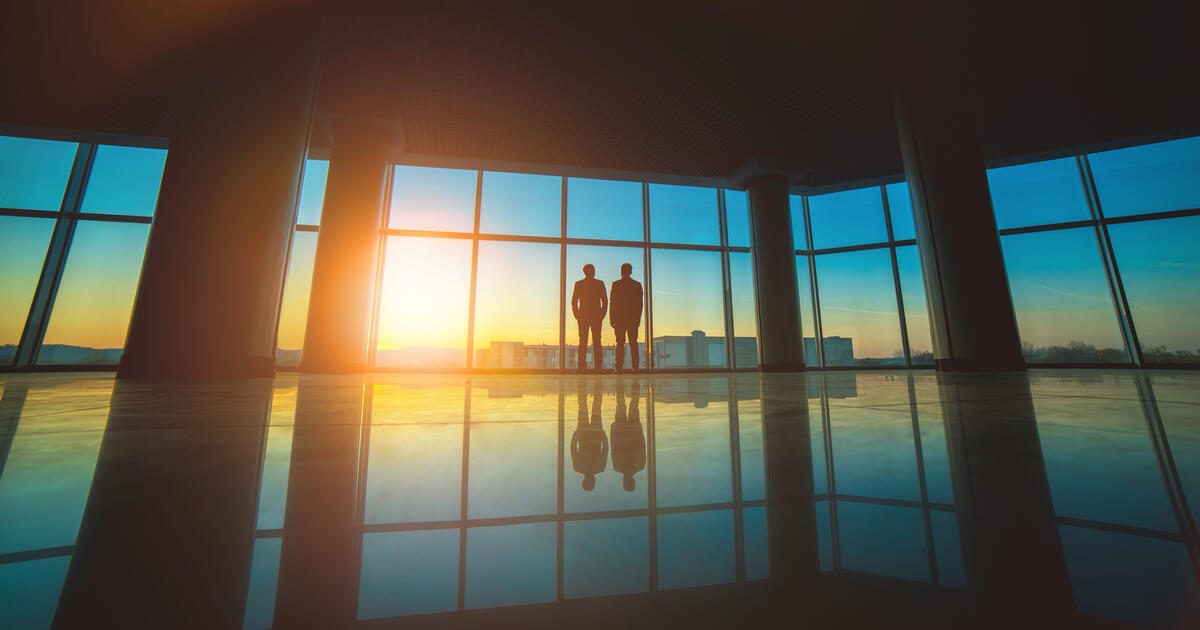 The two men stand near the panoramic window