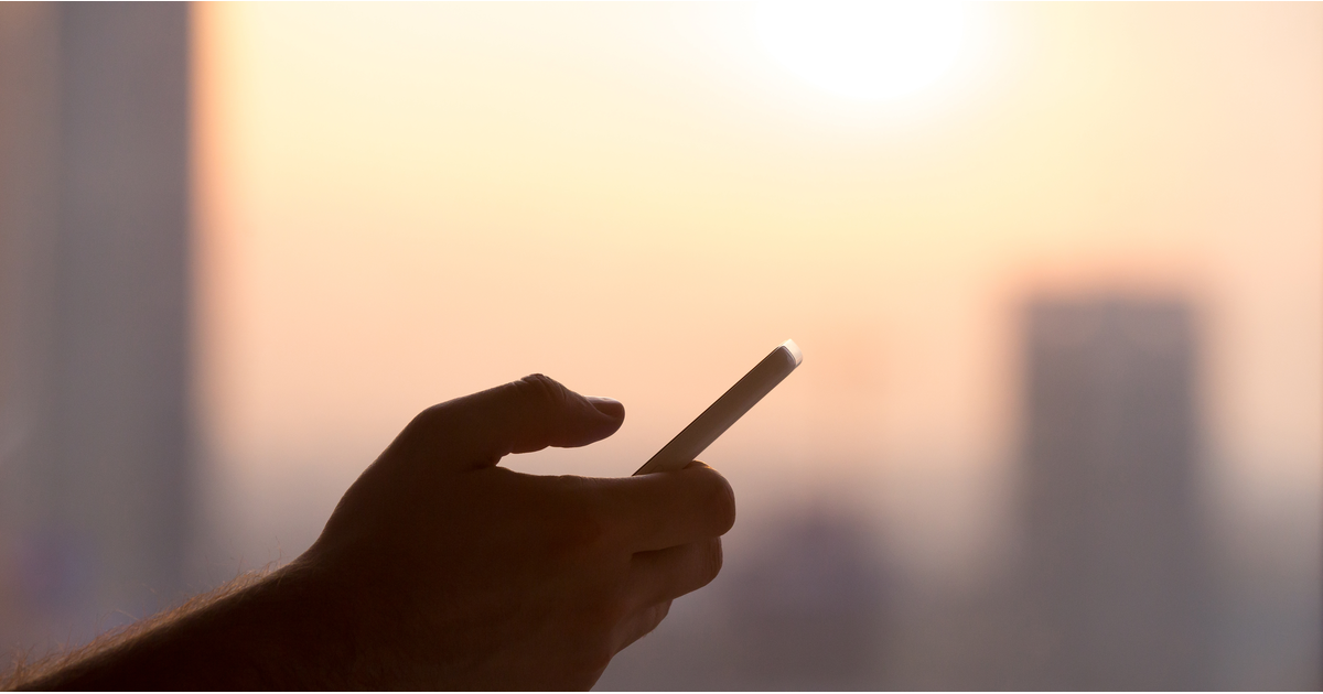 Handheld smartphone silhouetted against a bright sky