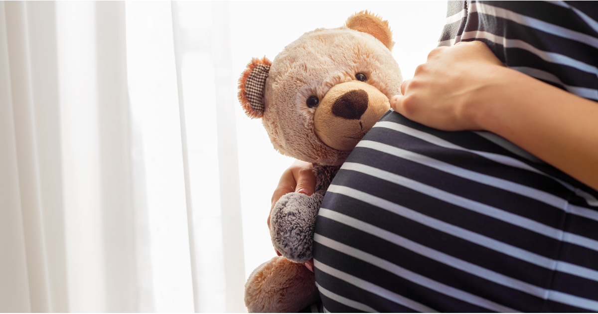 Pregnant woman sitting and holding teddy bear working parents-LinkedIn