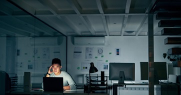 Male employee sitting at laptop in dark with worried expression