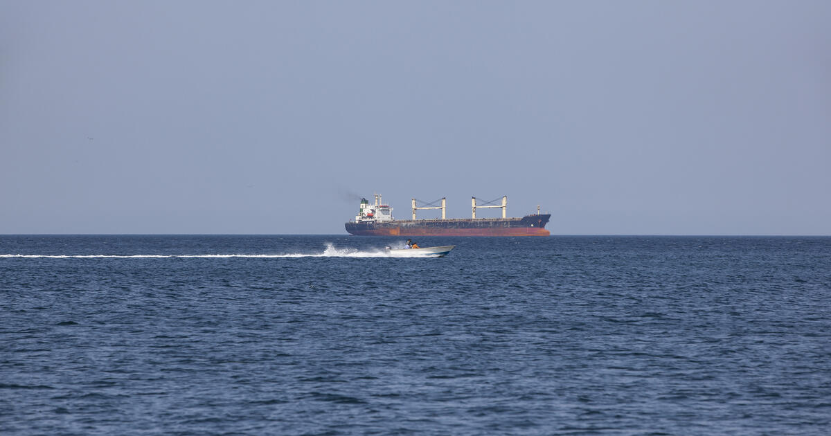 Large cargo vessel sailing in the Strait of Hormuz with a small speedboat passing in the foreground. The strategic waterway between Oman and Iran is one of the world’s most important maritime shipping routes.