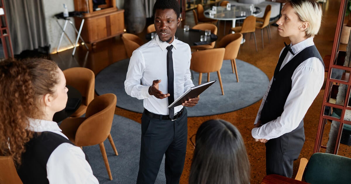 High angle portrait of restaurant manager talking to servers wearing classic uniforms during staff meeting in modern dining room