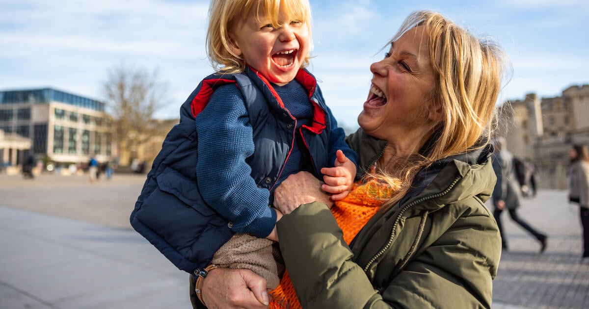 Grandmother holding her grandson, both laughing and enjoying a sunny day in the square near the Tower of London, showing family love and connection